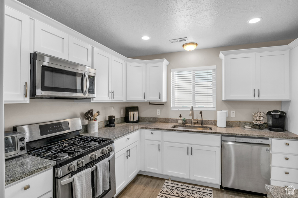 Kitchen with stainless steel appliances, a sink, white cabinets, a textured ceiling, and recessed lighting