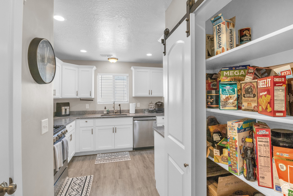 Kitchen with stainless steel appliances, a sink, white cabinets, a textured ceiling, and light wood-style flooring