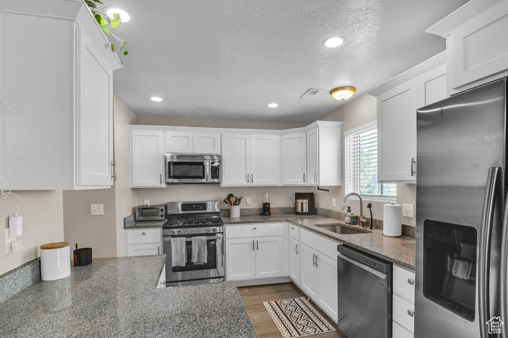Kitchen with appliances with stainless steel finishes, a sink, white cabinets, a textured ceiling, and recessed lighting