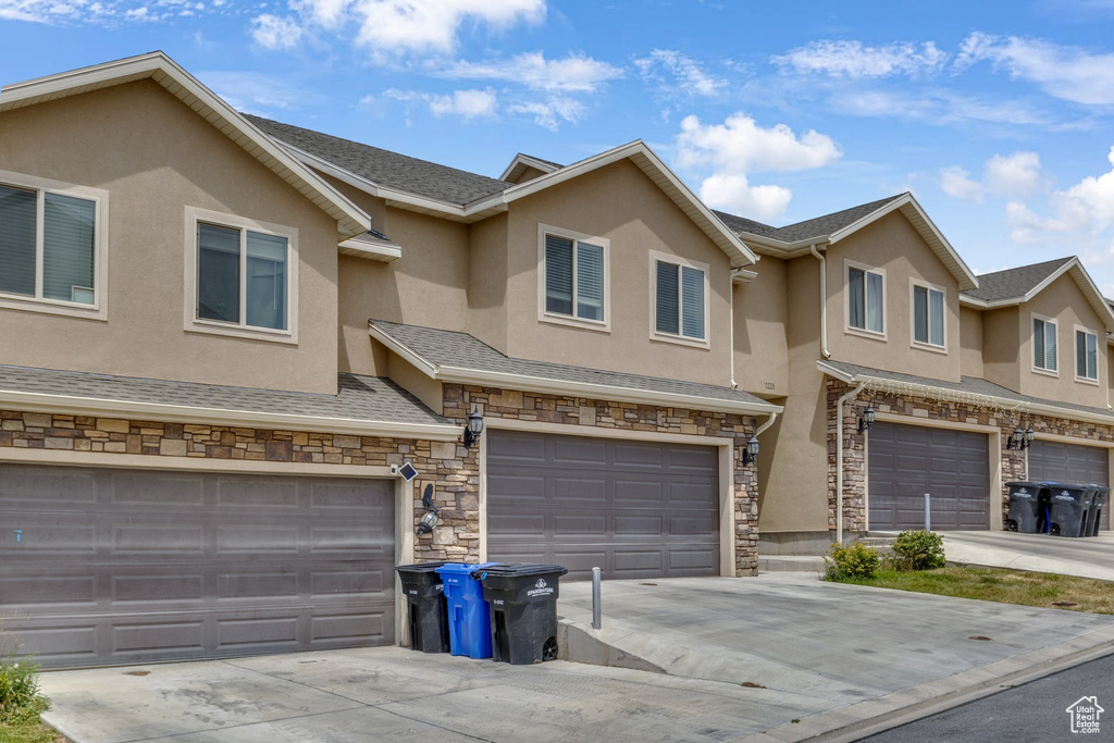 View of property featuring stucco siding, an attached garage, stone siding, and driveway
