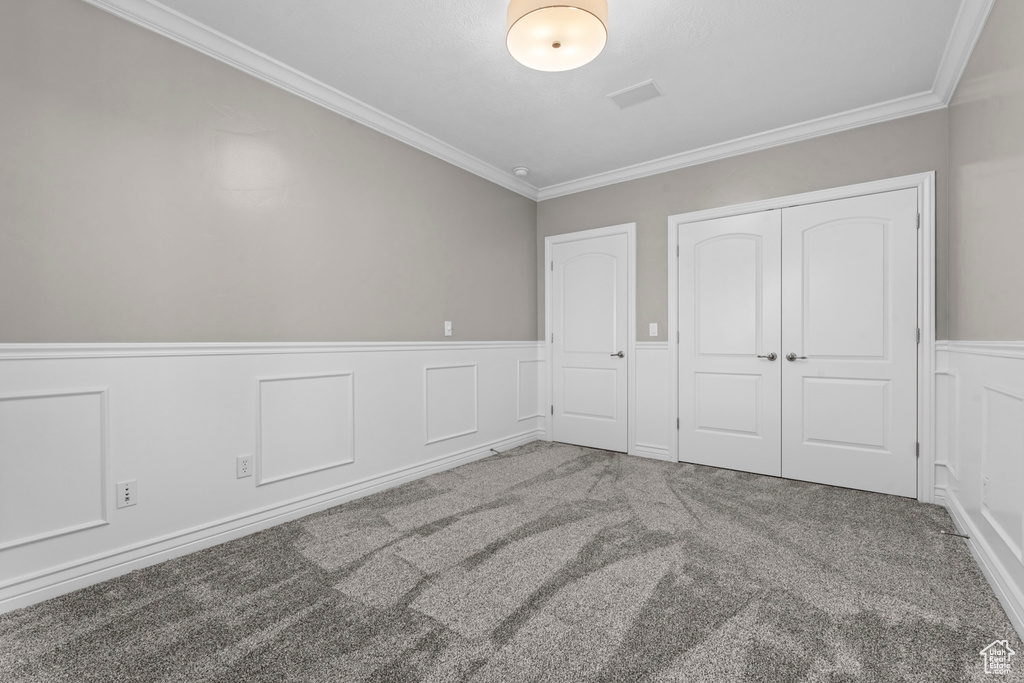 Unfurnished bedroom with carpet flooring, crown molding, wainscoting, a closet, and a decorative wall