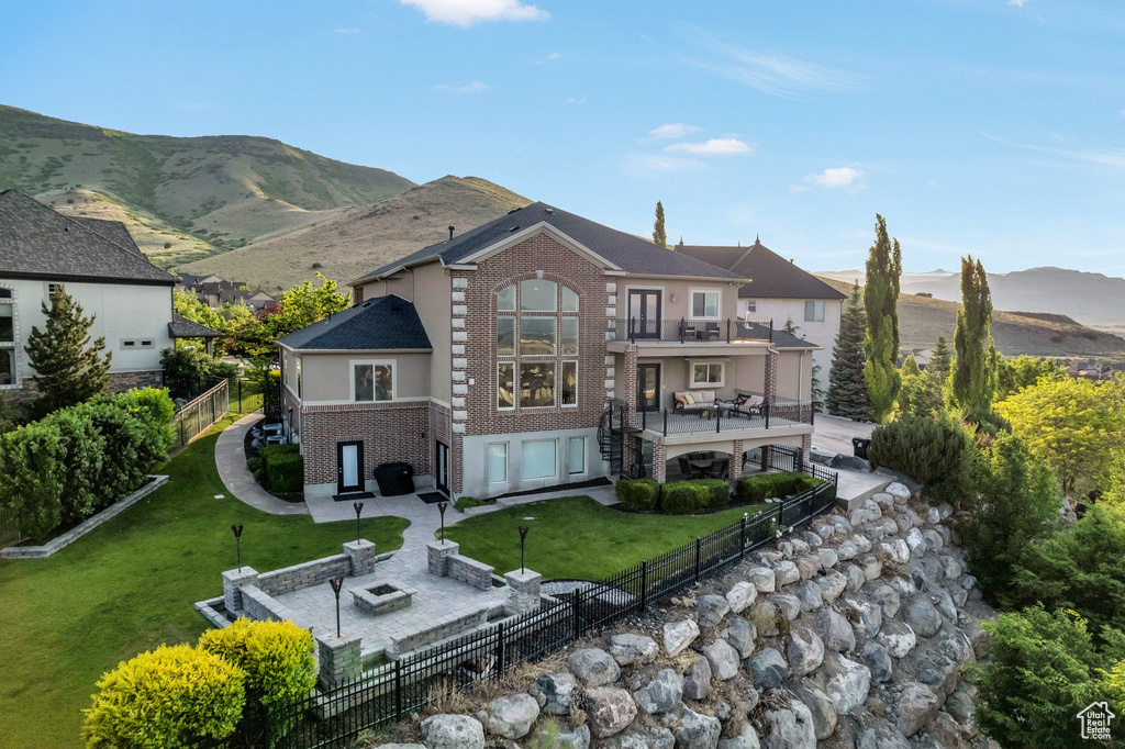 Back of house with a balcony, brick siding, a patio area, and an outdoor fire pit