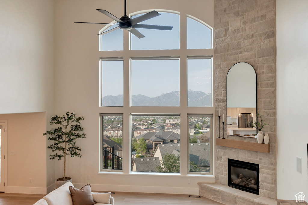 Living room featuring a towering ceiling, a ceiling fan, a mountain view, a stone fireplace, and wood finished floors