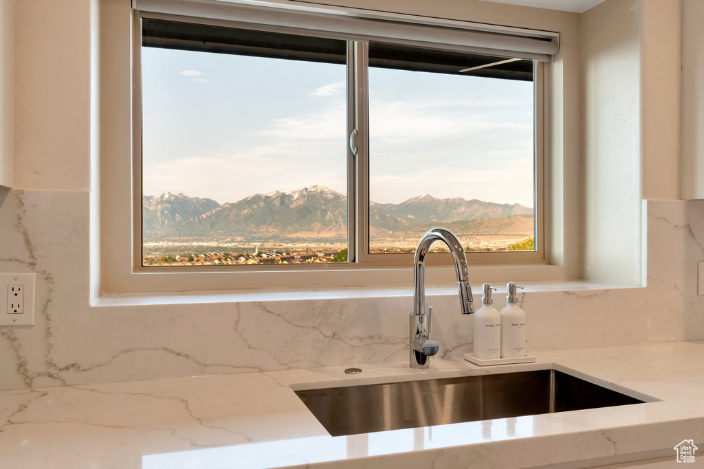 Kitchen view of a sink, backsplash, light stone counters, and a mountain backdrop