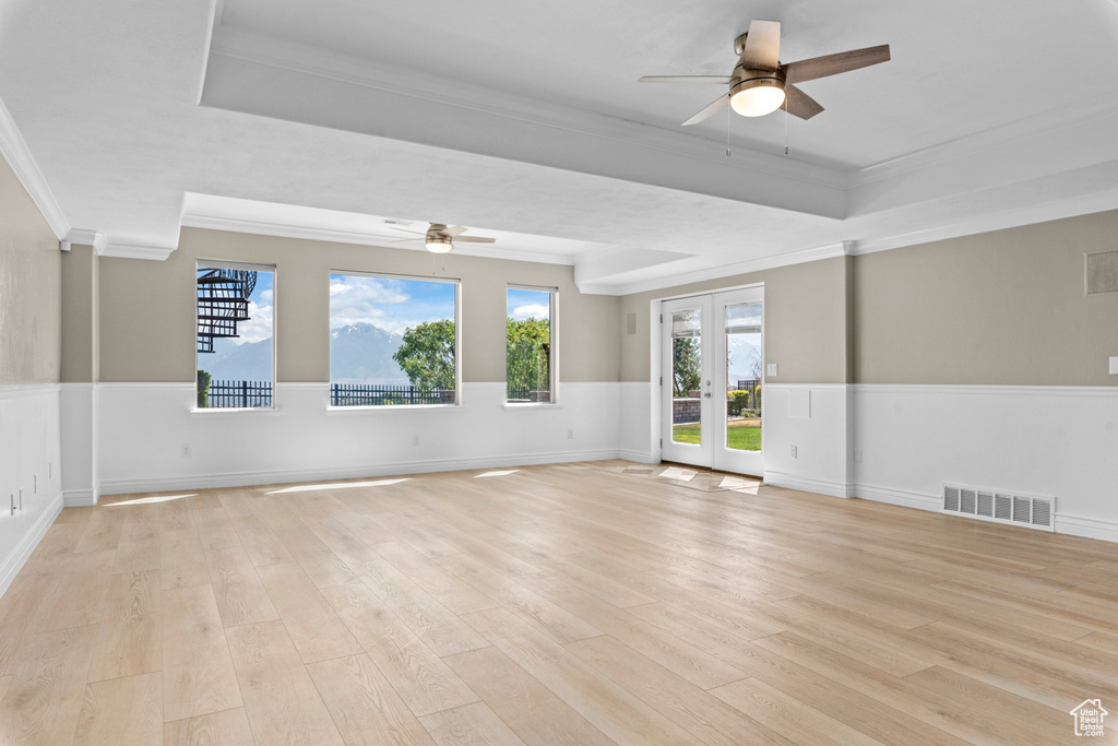Spare room with a ceiling fan, a tray ceiling, ornamental molding, light wood-style flooring, and plenty of natural light