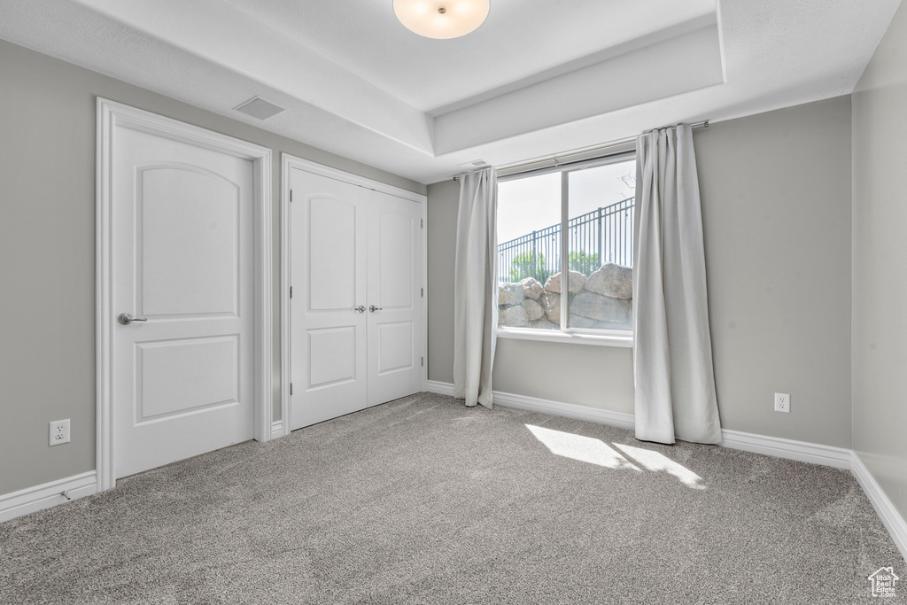 Unfurnished bedroom with carpet flooring, baseboards, and a tray ceiling