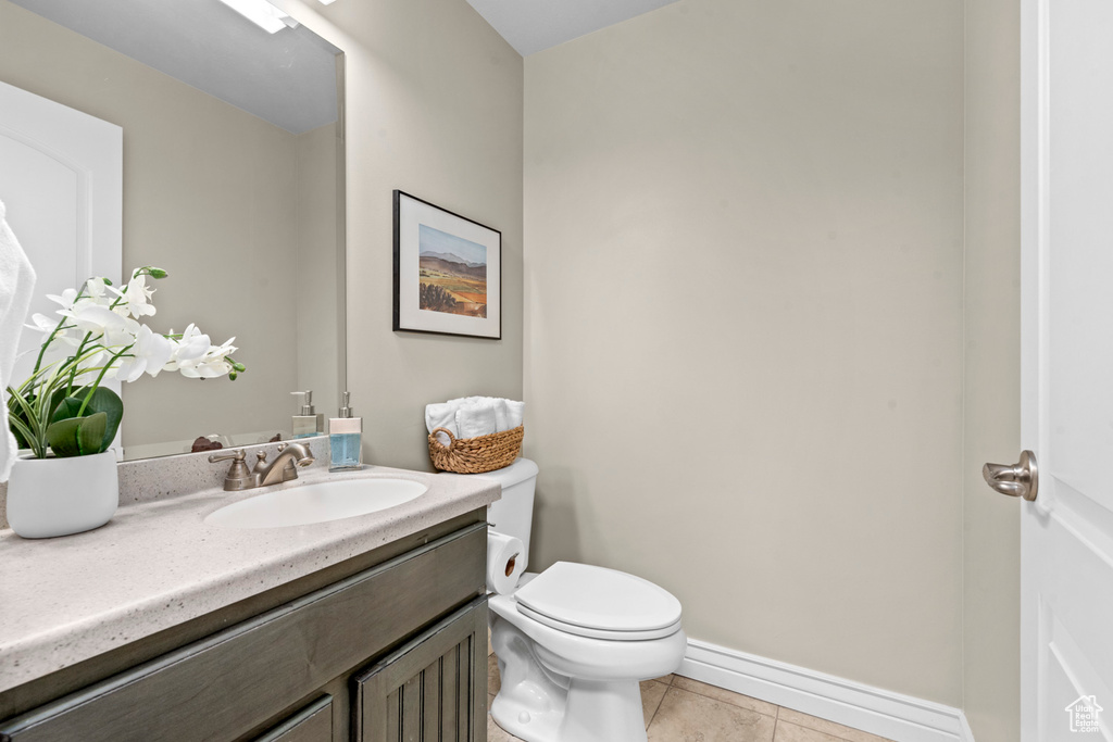 Half bath featuring toilet, vanity, tile patterned floors, and baseboards