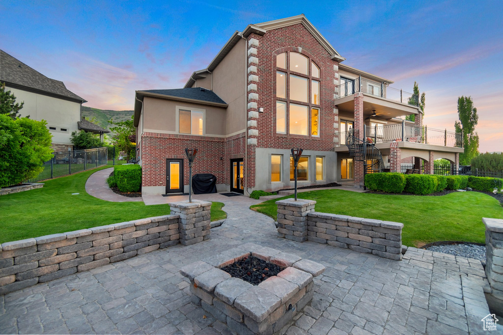 Back of house at dusk featuring a balcony, a patio, stairs, stucco siding, and a ceiling fan