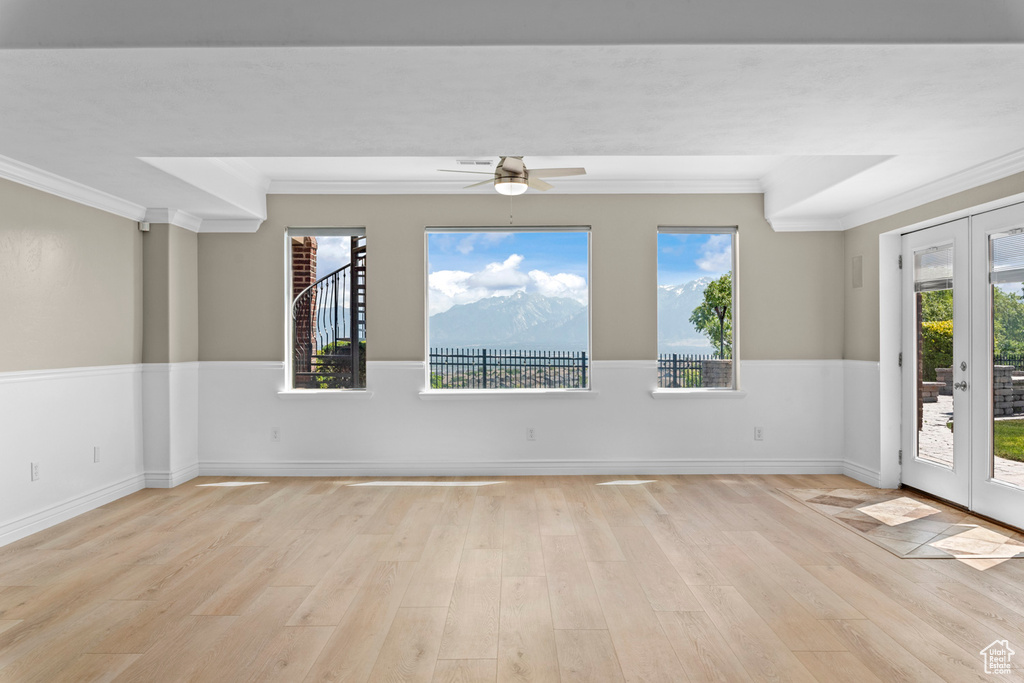 Empty room with ornamental molding, light wood-style floors, plenty of natural light, ceiling fan, and french doors