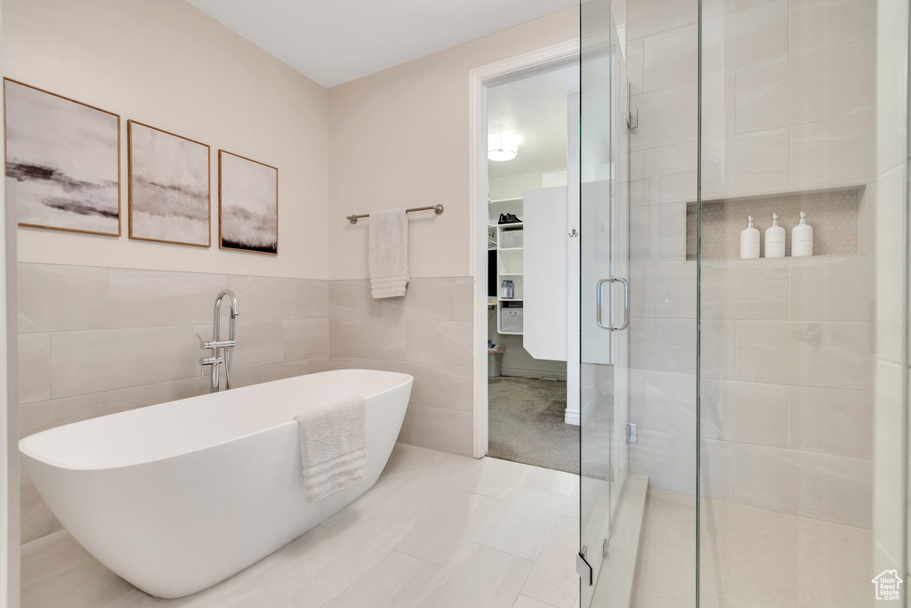 Bathroom featuring a stall shower, a soaking tub, a walk in closet, and tile walls
