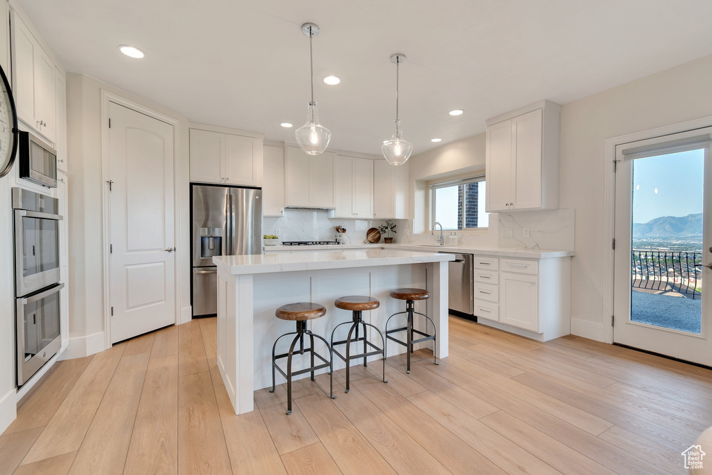 Kitchen with stainless steel appliances, a kitchen breakfast bar, white cabinetry, tasteful backsplash, and recessed lighting
