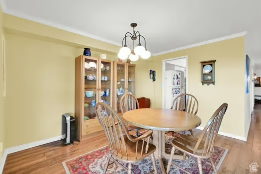 Dining room with wood finished floors, a chandelier, ornamental molding, and baseboards