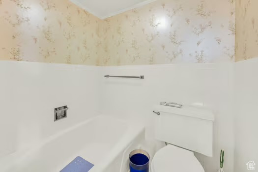 Full bath featuring wallpapered walls, toilet, a tub to relax in, and wainscoting