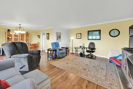 Living area with wood finished floors, a chandelier, crown molding, and baseboards