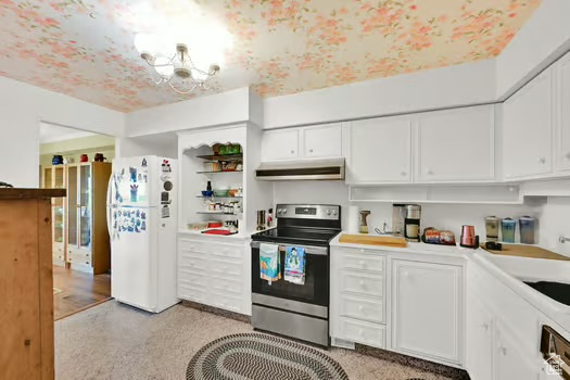 Kitchen with electric stove, freestanding refrigerator, under cabinet range hood, white cabinets, and a chandelier