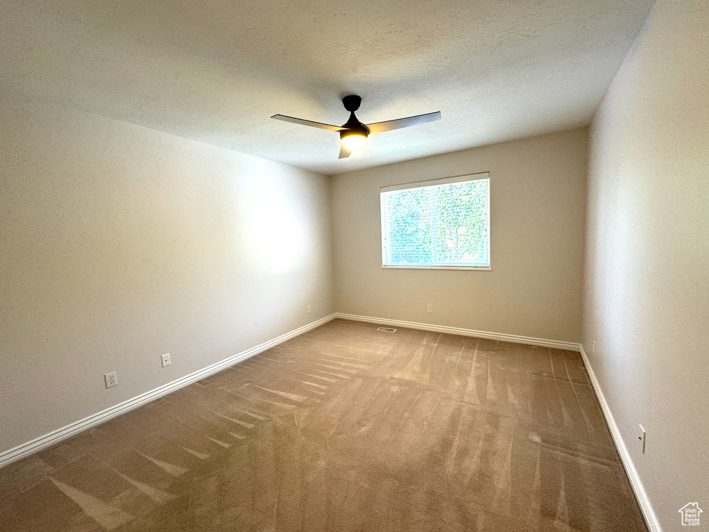 Carpeted spare room featuring a ceiling fan and baseboards