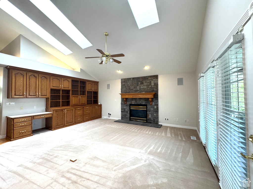 Unfurnished living room featuring a skylight, high vaulted ceiling, a stone fireplace, ceiling fan, and baseboards