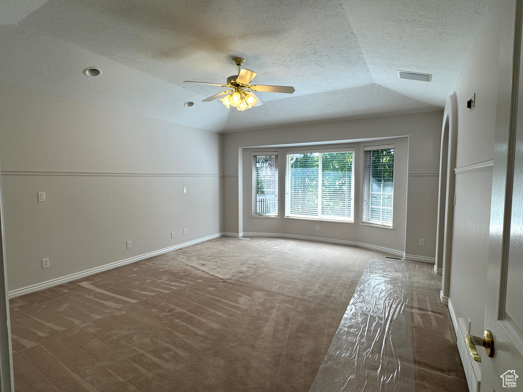 Carpeted empty room featuring ceiling fan, a textured ceiling, vaulted ceiling, and baseboards