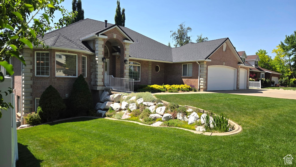 View of front of house featuring brick siding, a garage, driveway, a front yard, and roof with shingles