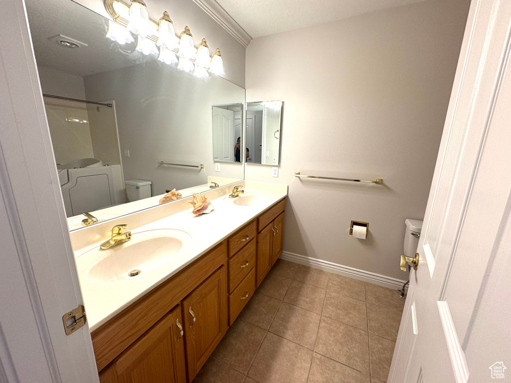 Bathroom with toilet, double vanity, baseboards, tile patterned floors, and a shower