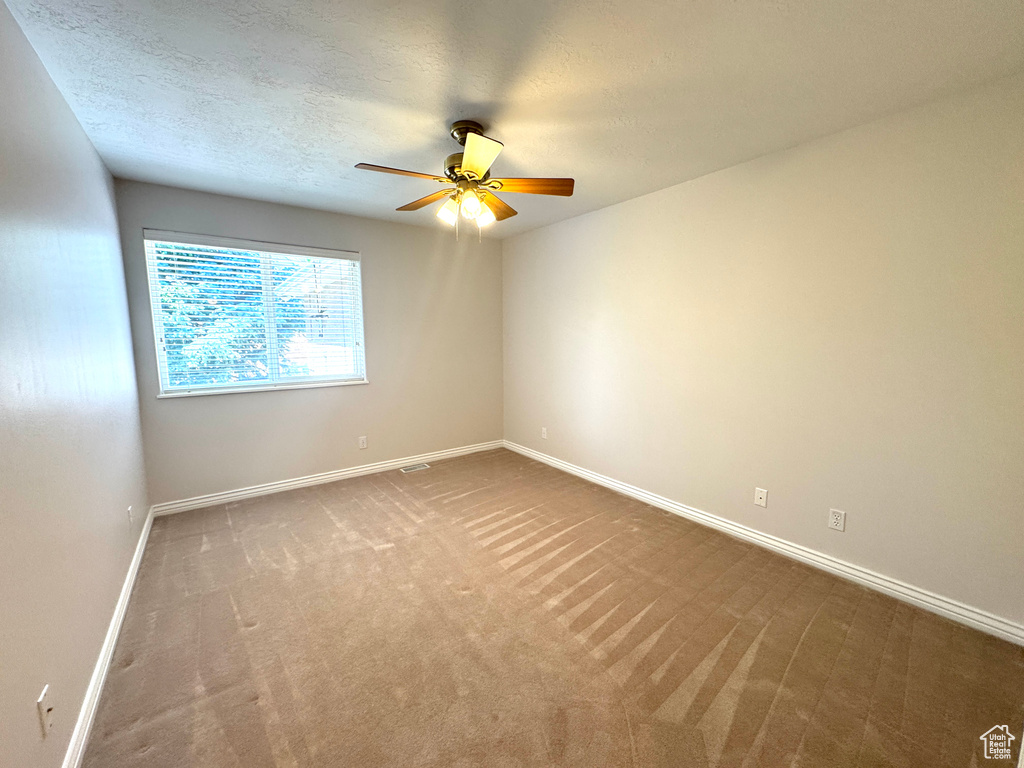 Carpeted empty room featuring ceiling fan, baseboards, and a textured ceiling