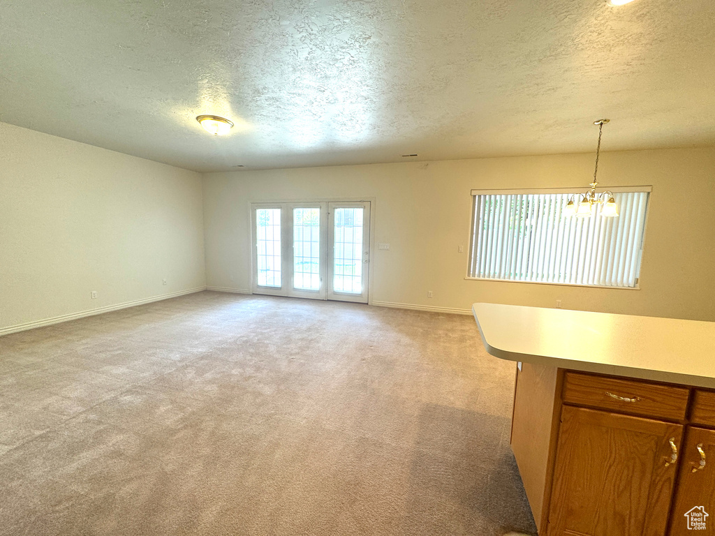 Unfurnished living room featuring a textured ceiling, baseboards, light colored carpet, and a chandelier