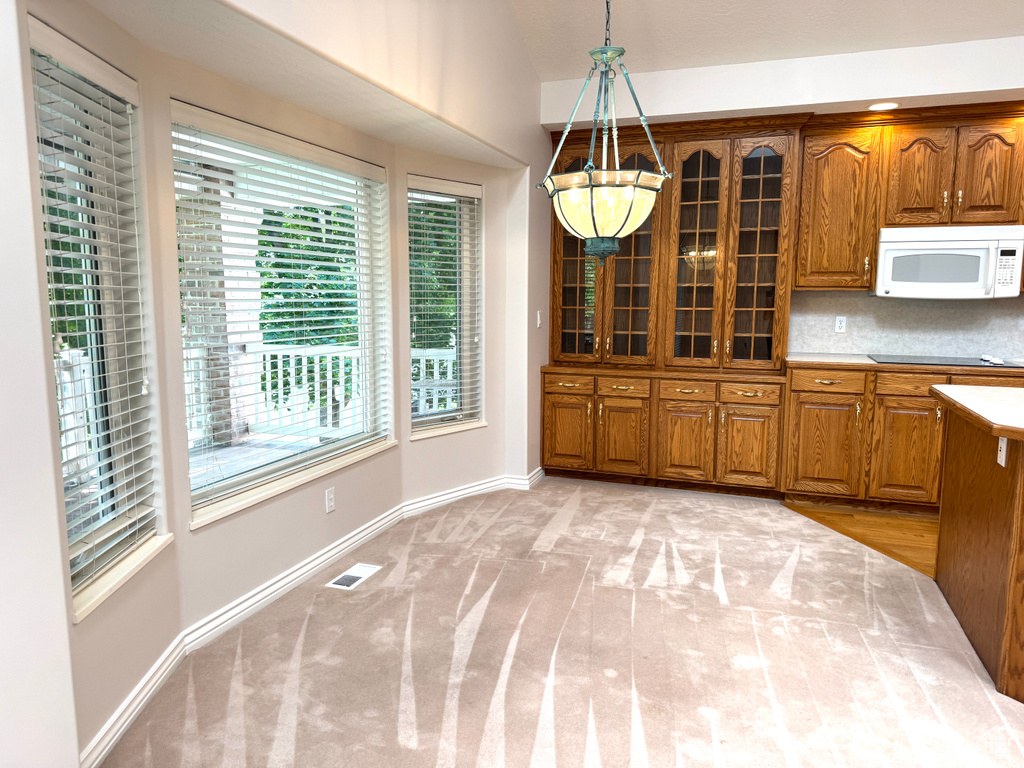 Kitchen with white microwave, brown cabinets, plenty of natural light, and glass insert cabinets