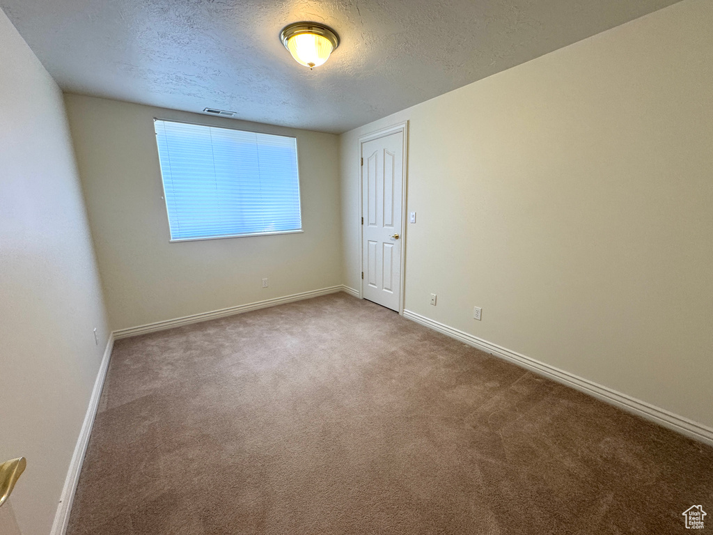 Spare room featuring baseboards, a textured ceiling, and carpet
