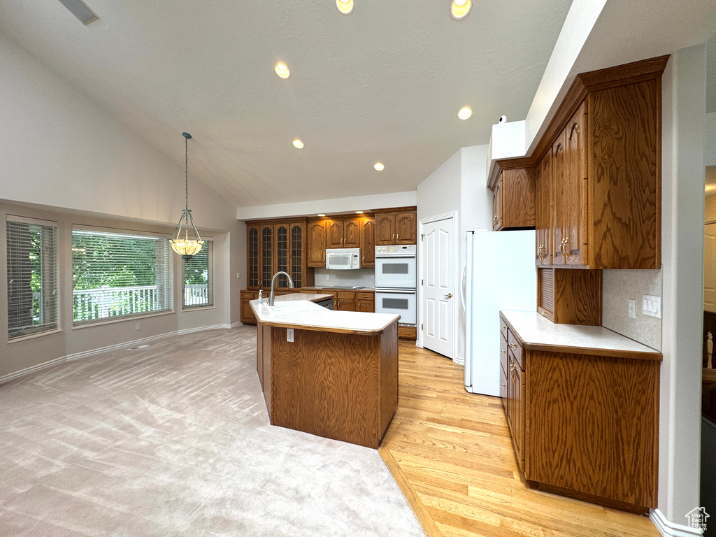 Kitchen with white appliances, brown cabinetry, a sink, recessed lighting, and light countertops