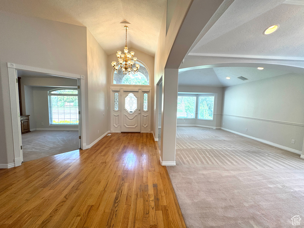 Foyer featuring lofted ceiling, plenty of natural light, arched walkways, baseboards, and a chandelier