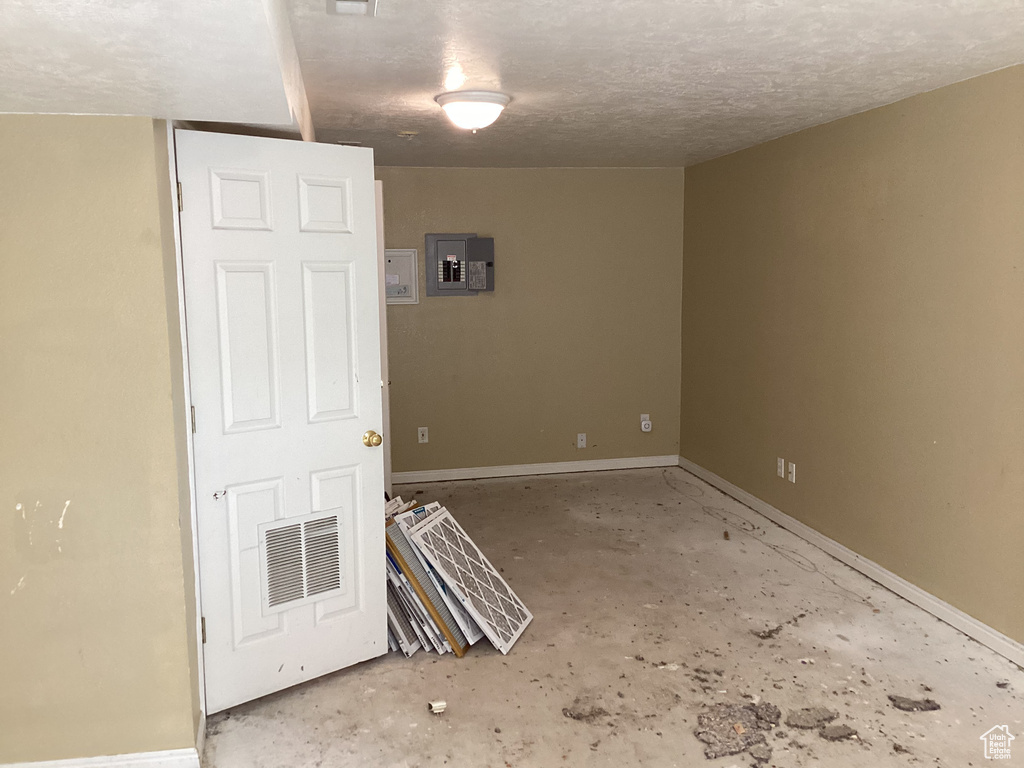 Spare room with baseboards, unfinished concrete floors, a textured ceiling, and electric panel