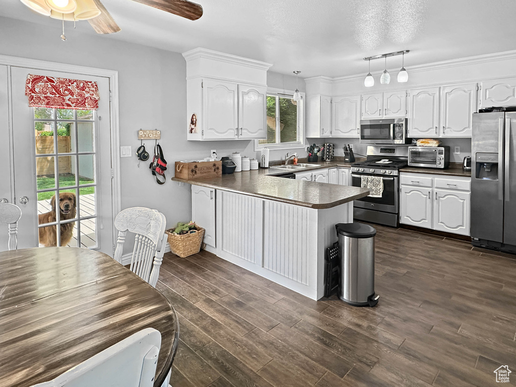 Kitchen with stainless steel appliances, a peninsula, dark countertops, and white cabinetry