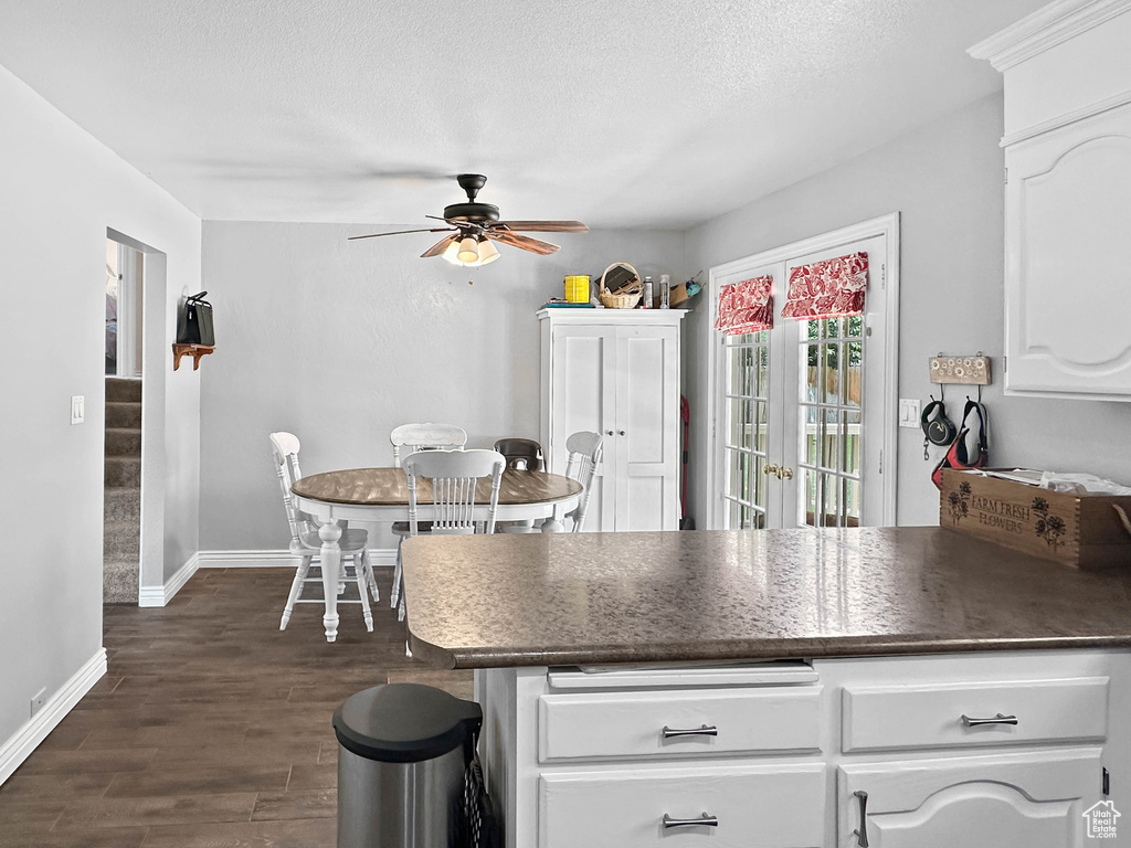 Kitchen with dark countertops, a ceiling fan, baseboards, dark wood-type flooring, and white cabinets