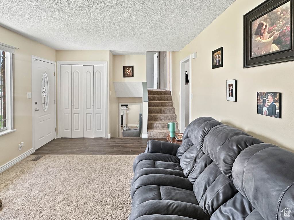 Living room with carpet, baseboards, a textured ceiling, and stairs