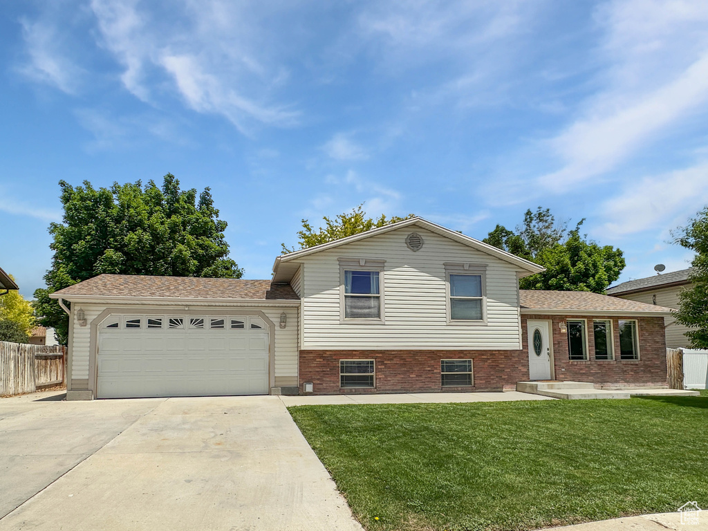 Split level home featuring driveway, a garage, and brick siding