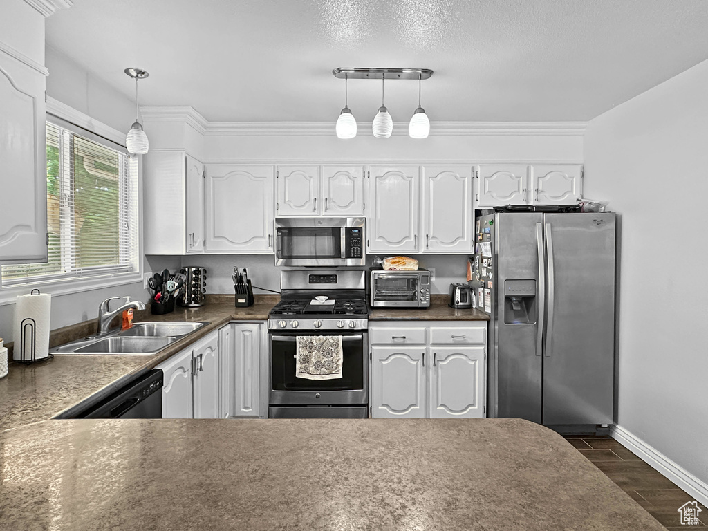 Kitchen with stainless steel appliances, a sink, dark countertops, white cabinets, and hanging light fixtures