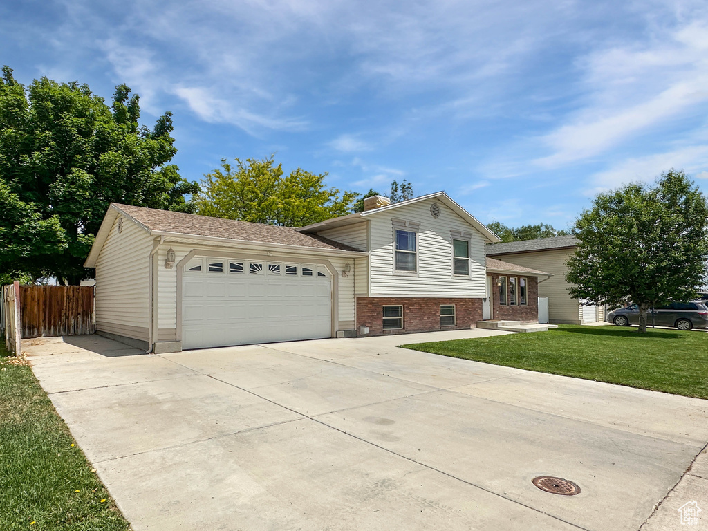 Tri-level home with concrete driveway, a garage, brick siding, and a chimney