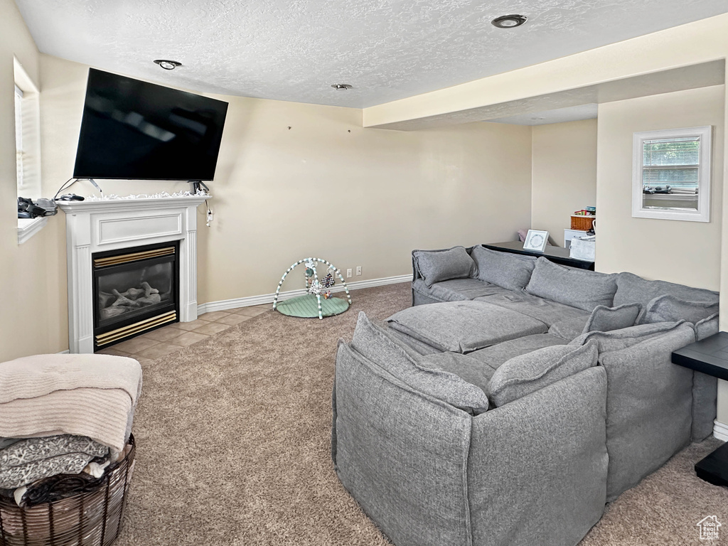 Living room featuring light carpet, a textured ceiling, baseboards, and a fireplace with flush hearth