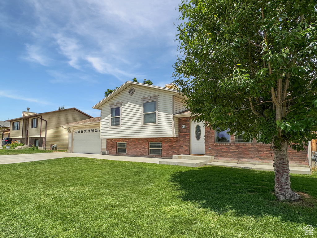 Split level home with brick siding, concrete driveway, a front lawn, and a garage