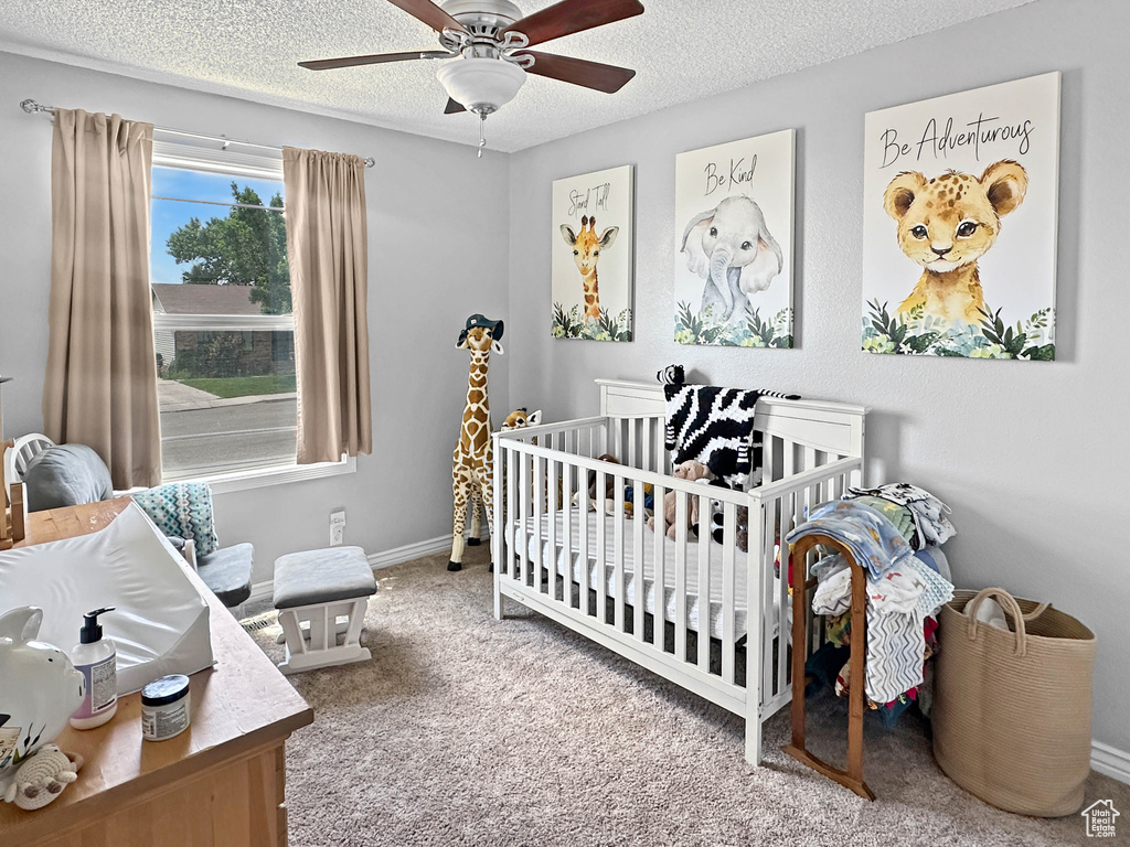 Carpeted bedroom with a textured ceiling, baseboards, a nursery area, and a ceiling fan