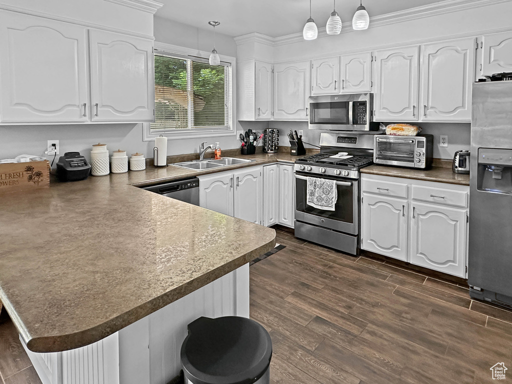 Kitchen with appliances with stainless steel finishes, a sink, a peninsula, white cabinets, and pendant lighting