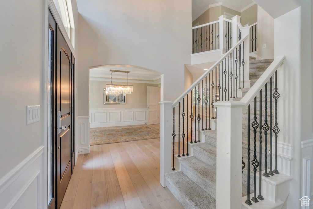Entrance foyer with arched walkways, a high ceiling, light wood-style flooring, stairs, and ornamental molding