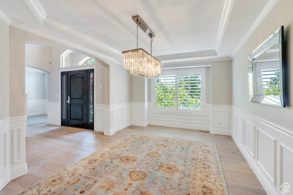 Spare room with a chandelier, a tray ceiling, arched walkways, light wood-style flooring, and wainscoting