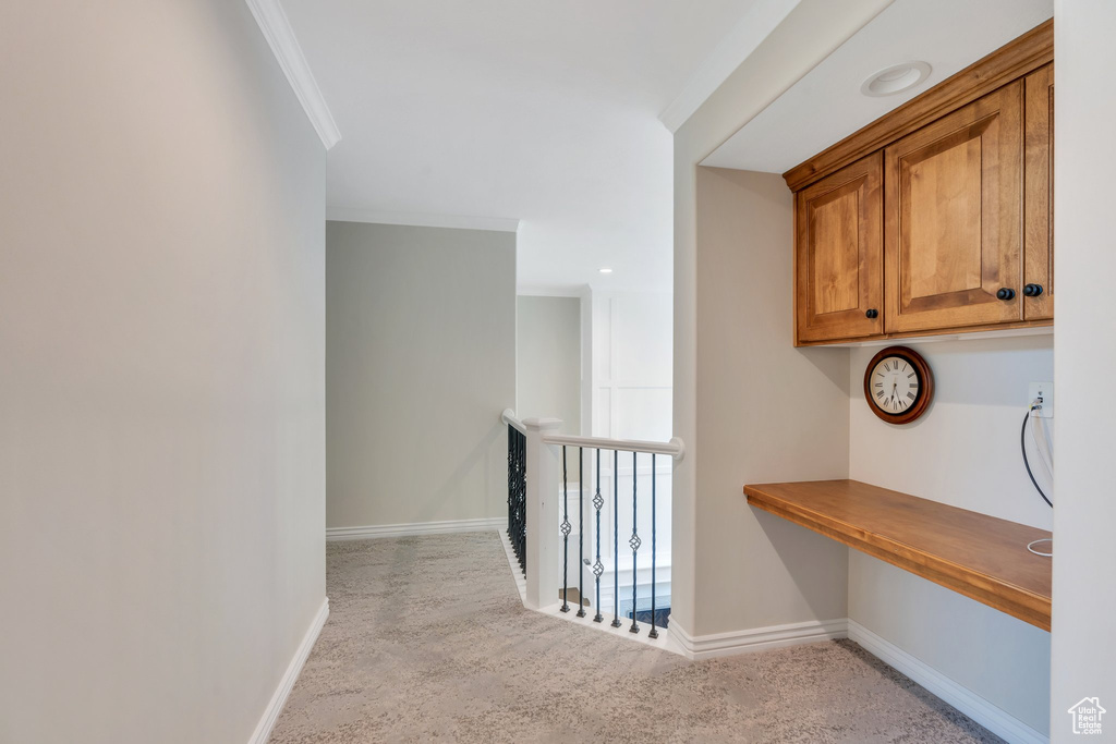 Hall with carpet, baseboards, crown molding, and a desk