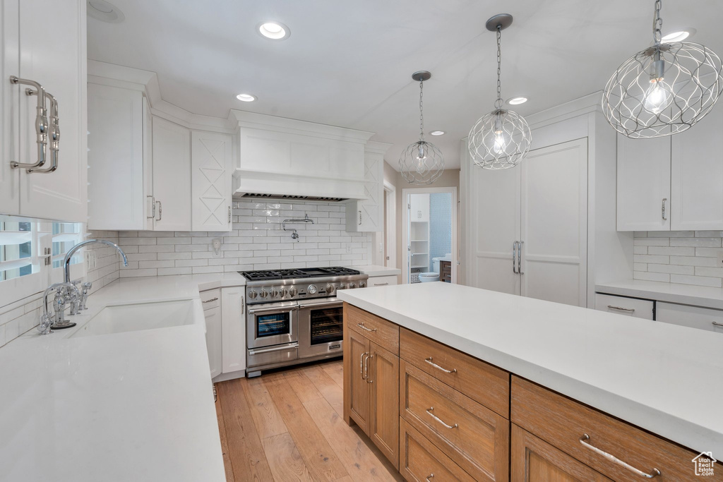 Kitchen featuring range with two ovens, custom exhaust hood, a sink, light countertops, and backsplash