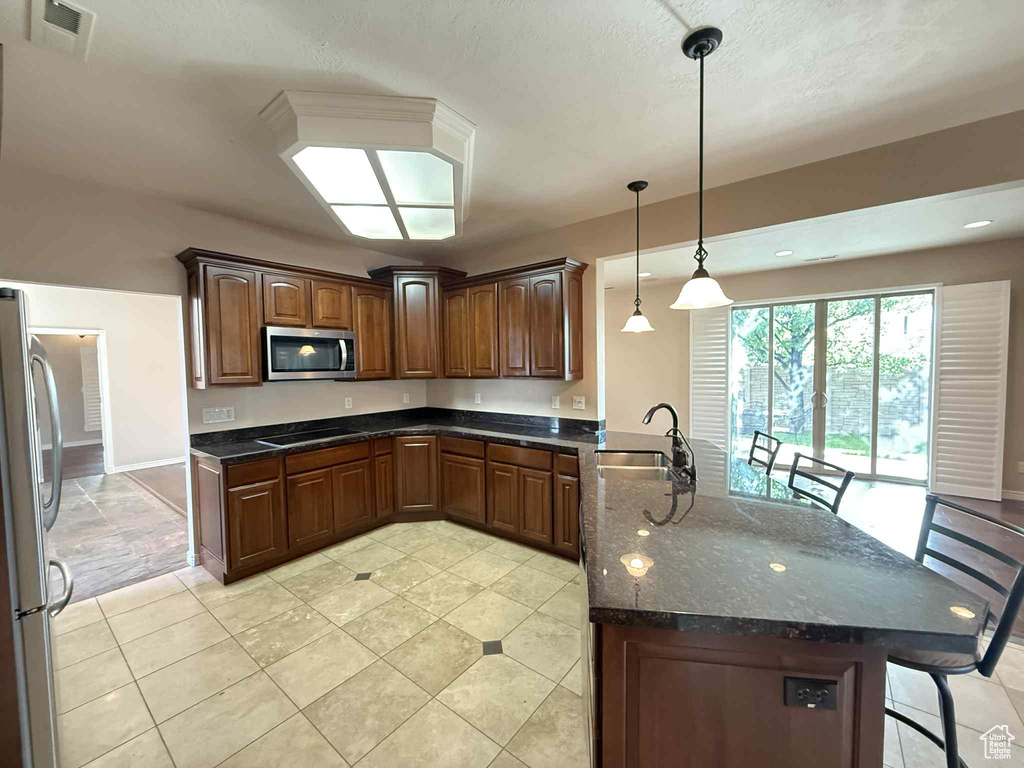 Kitchen featuring appliances with stainless steel finishes, a peninsula, a sink, a kitchen breakfast bar, and light tile patterned floors