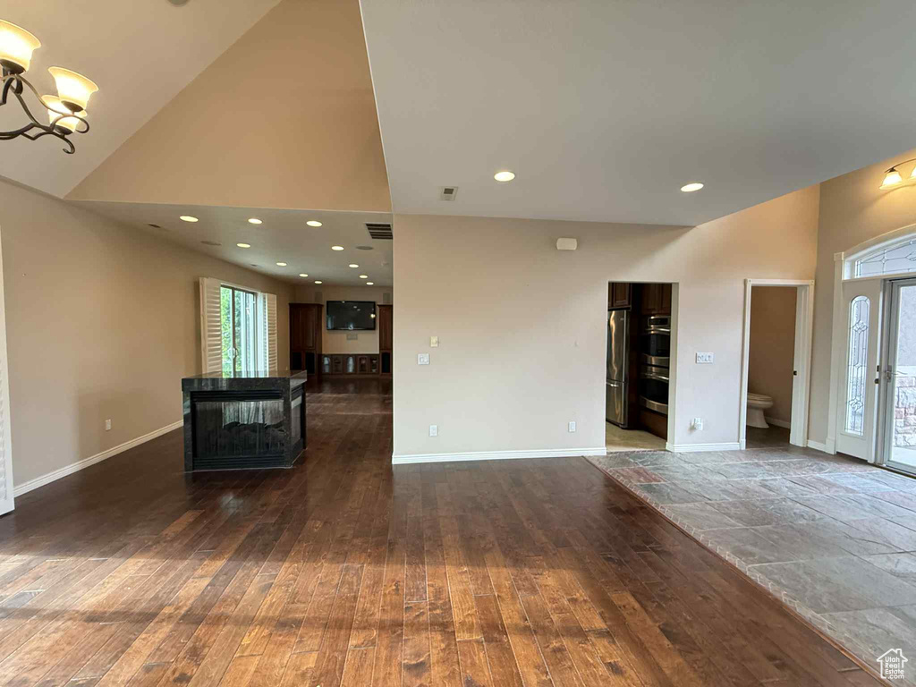 Unfurnished living room with a chandelier, wood-type flooring, a high ceiling, baseboards, and recessed lighting