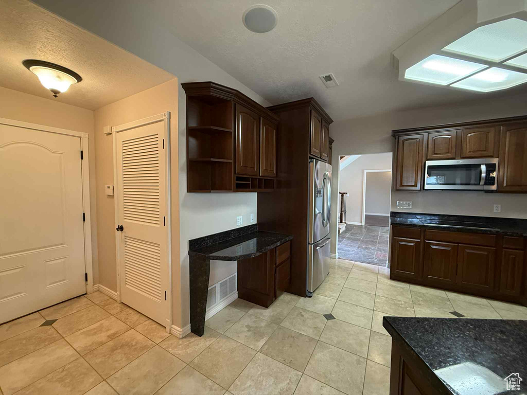 Kitchen featuring appliances with stainless steel finishes, light tile patterned flooring, dark brown cabinetry, and a textured ceiling