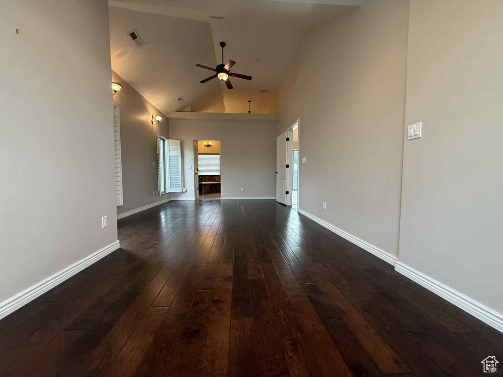 Unfurnished living room featuring dark wood finished floors, a ceiling fan, high vaulted ceiling, and baseboards