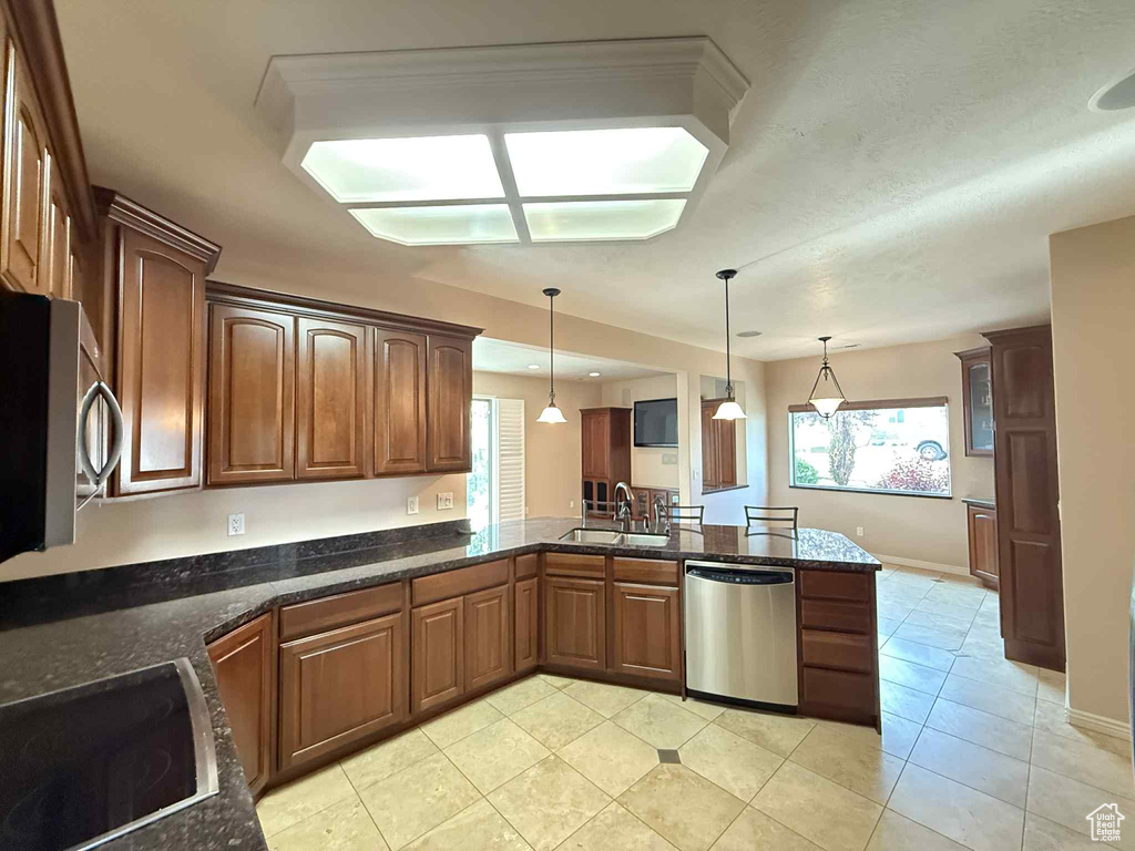 Kitchen with appliances with stainless steel finishes, a sink, a peninsula, light tile patterned flooring, and hanging light fixtures